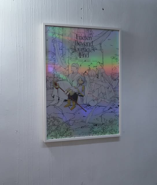 White-framed illustrated Frieren: Beyond Journey’s End poster with a rainbow sheen on a pale wall.