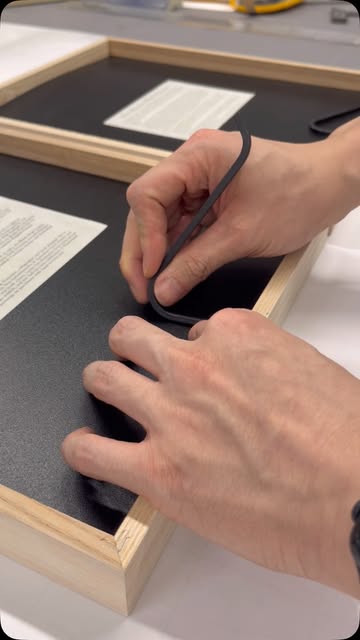 Hands working on the black backing of a wooden picture frame.