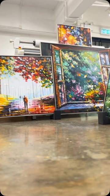 Colorful framed paintings propped on a workshop floor.